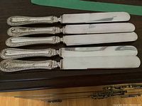 Five sterling silver handled dinner knives laid out on a wooden surface.
