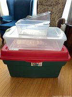Four plastic storage bins stacked: large green RoughTote bin with red lid on bottom, medium clear bin with white lid in middle, two smaller clear bins on top without lids.