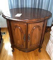 Top and front view of round wood side table with storage cupboard. Shows wood grain finish and decorative handles.