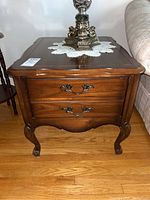 Front view of wooden side table showing two drawers with decorative metal handles, slight surface wear and polished finish.