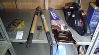 Tools on shelf including hedge trimmer, tree limb looper, handsaw, and drill bit set.