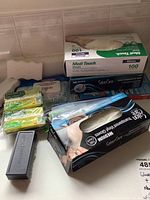 Wide view of the lot showing three boxes of vinyl gloves, multiple packs of cleaning sponges in different colors, and a black plastic case.