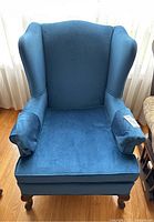 Front view of blue velvet wing back chair showing seat, arms, and backrest upholstery.