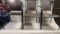 Front-facing view showing the set of three woven wicker chairs with black metal tubular frames and armrests.