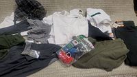Full view of various new clothing items including tops, bottoms, and sock package laid out on a light carpeted surface.