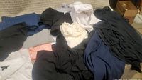 Pile of mixed colored tops and shirts including black, navy blue, white, cream, gray, and blue checkered.
