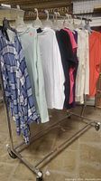 Metal garment rack holding 7 garments including blue plaid dress and varied colored tops and dresses.