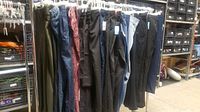 Nine pairs of pants hanging on a rack in various colors and styles, all new with tags attached.