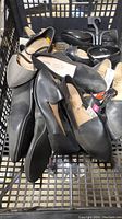 A shopping basket containing approximately 7 pairs of new women's shoes in various styles and sizes, mostly black and gray.