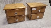 Pair of small solid wood drawer units with two metal knob handles each, displayed side by side on a carpeted surface.
