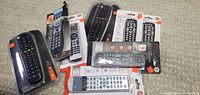 Photo showing multiple universal remotes, some in packages, some loose, mostly black with various button designs.