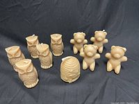 Photo showing six owl-shaped beeswax candles, four bear-shaped beeswax candles, and one beehive-shaped beeswax candle arranged on a black surface