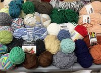Photo showing a wide variety of yarn skeins in assorted colors and brands including green, teal, peach, brown, and variegated patterns.