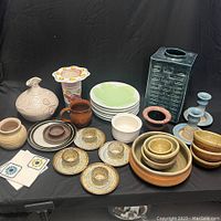 Full view of the assorted pottery lot displayed on black fabric background showing all items in the collection including plates, bowls, candlesticks, and decorative vessels.