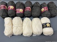 Twelve skeins of yarn arranged in two rows, six dark grey skeins on top and six cream white skeins on bottom, showing full lot contents.