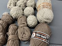 Balls and skeins of brown and beige 100% wool yarn, some with visible Patons Rustic Wool and Peer Gynt labels.