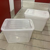 Two clear plastic storage bins with lids placed on floor, showing front and side view.