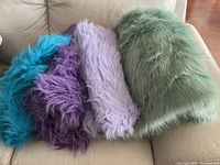 Four different colored faux fur fabric pieces laid out on a couch in turquoise, purple, light lavender, and mint teal colors.