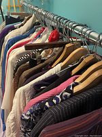 Closely hung vintage women's clothing on metal rack, showing various blouses, dresses, and jackets predominantly in classy prints and textures with colors including white, pink, purple, and metallic tones.