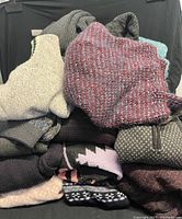Pile of folded knit sweaters showing variety of colors and knit styles including ribbed, patterned, and solid knits.