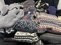 Overview of knit sweater lot showing various patterned and plain knit sweaters folded and stacked.