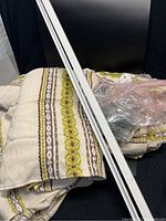 Woven curtain panels with geometric olive green and brown patterns on cream fabric, paired with two white curtain rods and plastic-wrapped hooks.