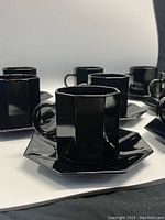 Eight black octagonal cups on matching octagonal saucers, arranged in rows on a white surface with black background.