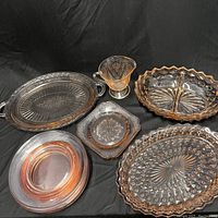 Overview of pink depression glass items including divided dish, creamer, trays, and plates.