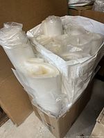 Multiple rolls of translucent plastic bags in a large white container, including types with zipper closures and adhesive strips.