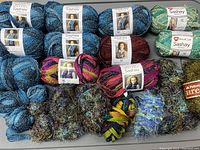 Overview of 15 skeins of Sashay yarn in various colors and metallic/sequined textures.