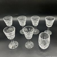 All seven glasses in the set arranged showing the shot glass and six stemmed liqueur glasses with signature Lismore cuts.