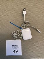 Apple AirPods charging case with white USB charging cable coiled and tied. The USB-A connector is visible. The case shows some minor signs of use.