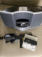 Portable Sirius/XM satellite radio system showing front with attached detachable receiver and remote, power adapter, user manual laid on a beige fabric surface.