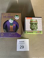 Full view of boxed Joker wooden figure and boxed Michelangelo Geeki Tiki mini mug with auction lot number in front.