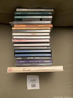 Stack of approximately 16 music CDs showing a mix of titles including Paul Simon - Graceland and American Folk The New Generation. Cases appear mostly jewel cases and various colors.