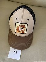 Baseball hat showing front panel with Tasmanian Devil face patch, brown brim, and black mesh back