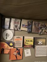 Top view of 14 CDs in jewel cases showing album artwork including INXS, R.E.M., Fleetwood Mac, Moist, Romeo + Juliet soundtrack, Barenaked Ladies, Depeche Mode, The Police, and OneRepublic.