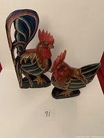 Photo showing both wooden rooster statues together, detailing their sizes and painted features.