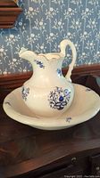 Photo showing ceramic white bath basin with blue floral designs and some gold edging, holding matching pitcher with similar decoration