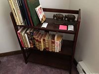 Full view of the bookcase showing three shelves holding books and small decor items. The carpet and lower wall trim are visible.