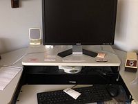 Dell computer workstation with monitor, keyboard, mouse, speaker and clock arranged on a desk stand.