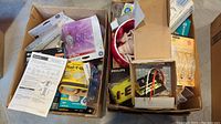 Two open cardboard boxes containing various light bulbs in packages and a Honeywell universal transformer in its original box along with instruction manual.