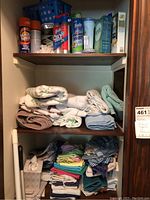 Three-shelf linen closet with folded washcloths, dishcloths, and cleaning products on top shelf