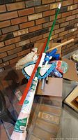 Lot showing two mops including a Libman Wonder Mop with white and orange mop head, several shorter mop heads/dusters in blue, red yard stick, unopened glove package, assorted bottles of cleaning and backyard chemicals on a table.