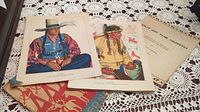 24 colorful Native American prints illustrating Blackfeet Indians and cultural attire spread on a table.