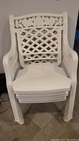 Stacked view of three white plastic chairs showing lattice backrest and rose design detail on top.