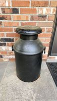 Front view of vintage black painted metal milk can showing overall shape and lid.