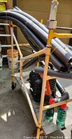 Yellow metal scaffold on wheels with black Echo backpack blower underneath and black pipe insulation stacked on top.
