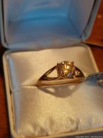 Close-up image of the gold plated sterling silver ring with a 1.45 carat round moissanite gemstone, shown inside a white ring box on satin.