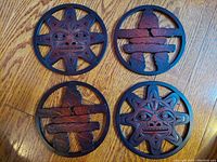 Photo of four BOMA crafted Indigenous imagery trivets on wooden floor, showing two Inukshuk and two sun mask designs.